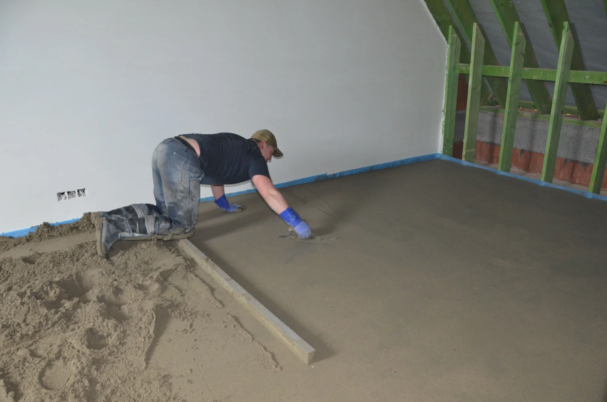 Vakman werkt een chape af op een zolderverdieping, met een randstrook langs de muur